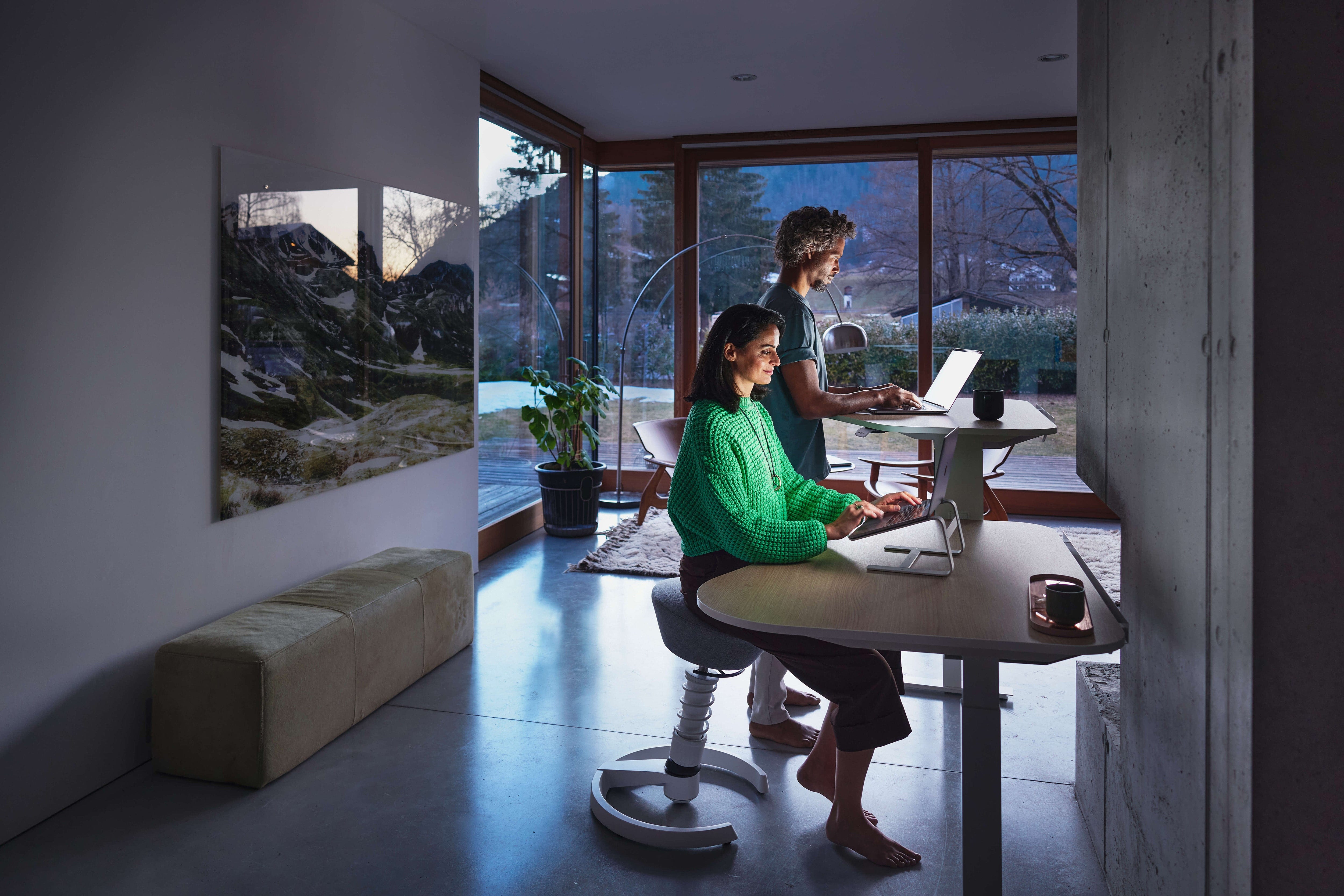 Zwei Personen arbeiten an einem ergonomischen Schreibtisch bei Abenddämmerung, wodurch sie ihre Produktivität steigern.